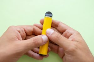 Mains tenant une cigarette électronique jaune