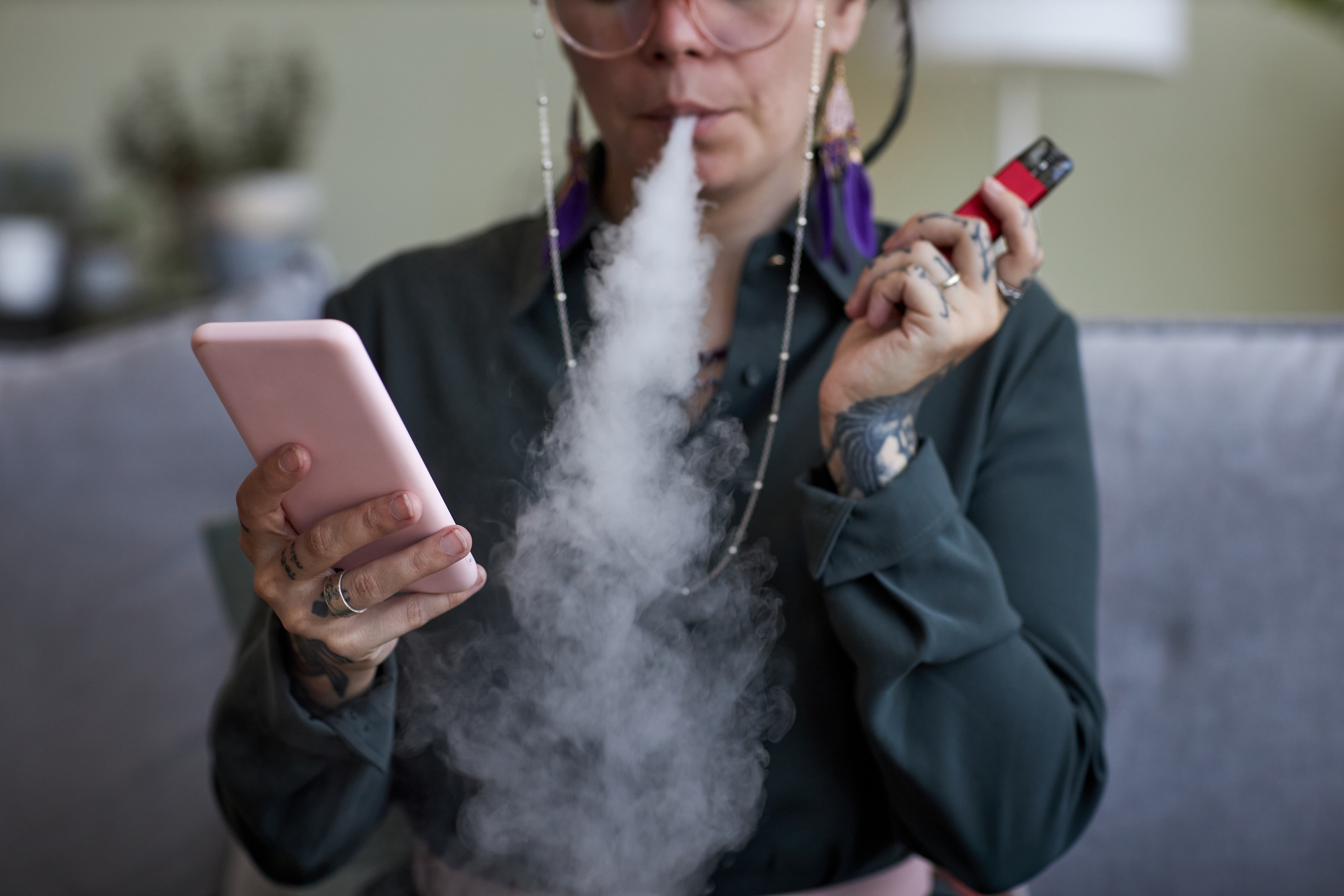 Close-up of young woman with e-cigarette using smartphone
