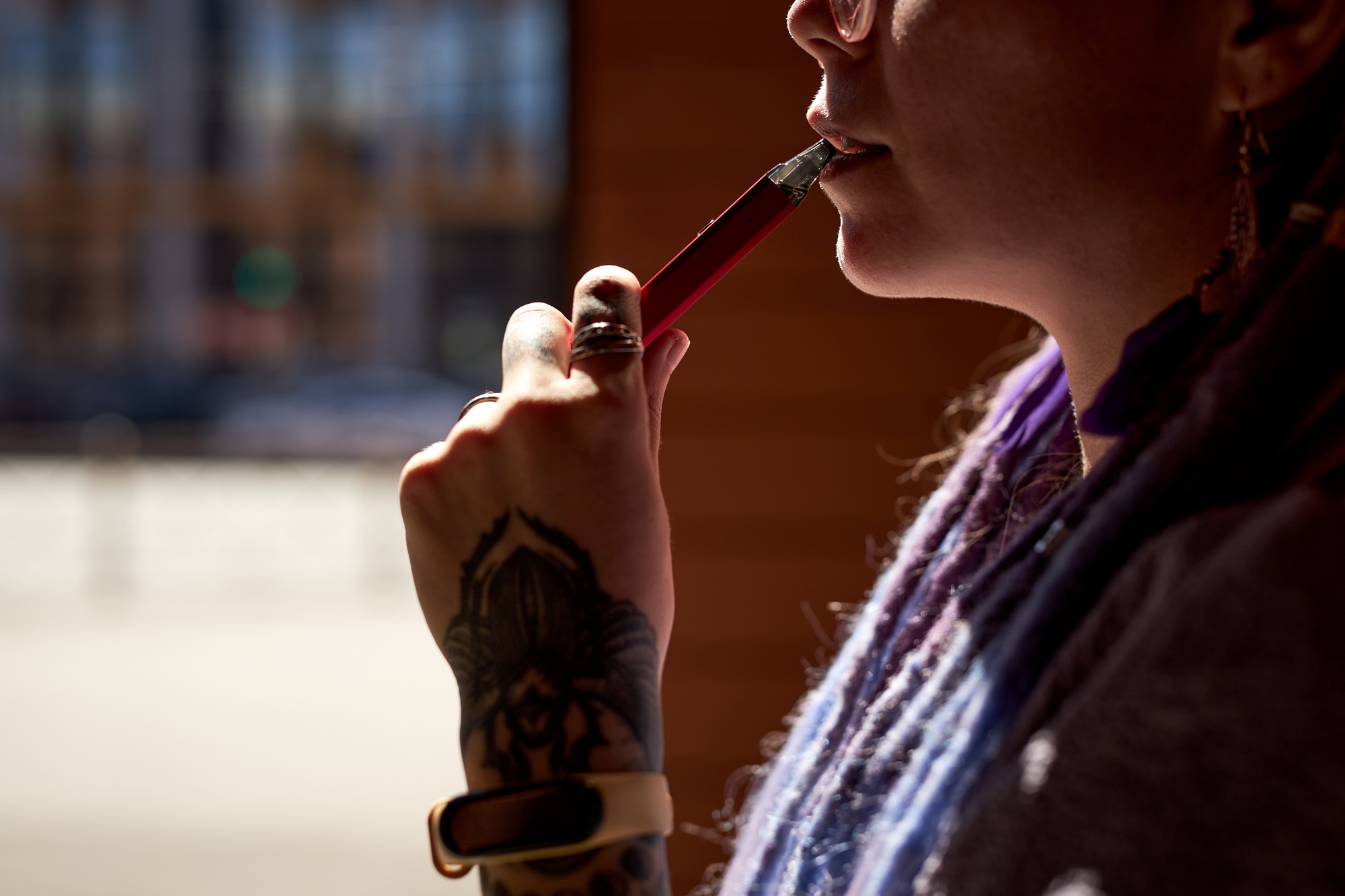 Close-up of young woman with tattoo on hand holding electronic cigarette
