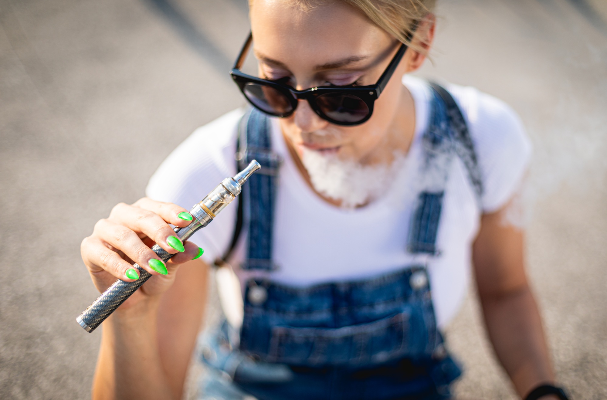 Modern woman outdoor smoking e-cigarette while sitting at city street